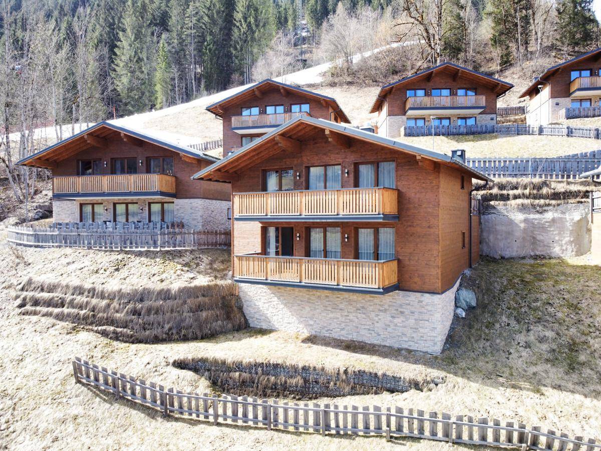 Mehrere moderne Chalets mit Holzfassaden und Balkonen, eingebettet in eine grüne Hanglandschaft.