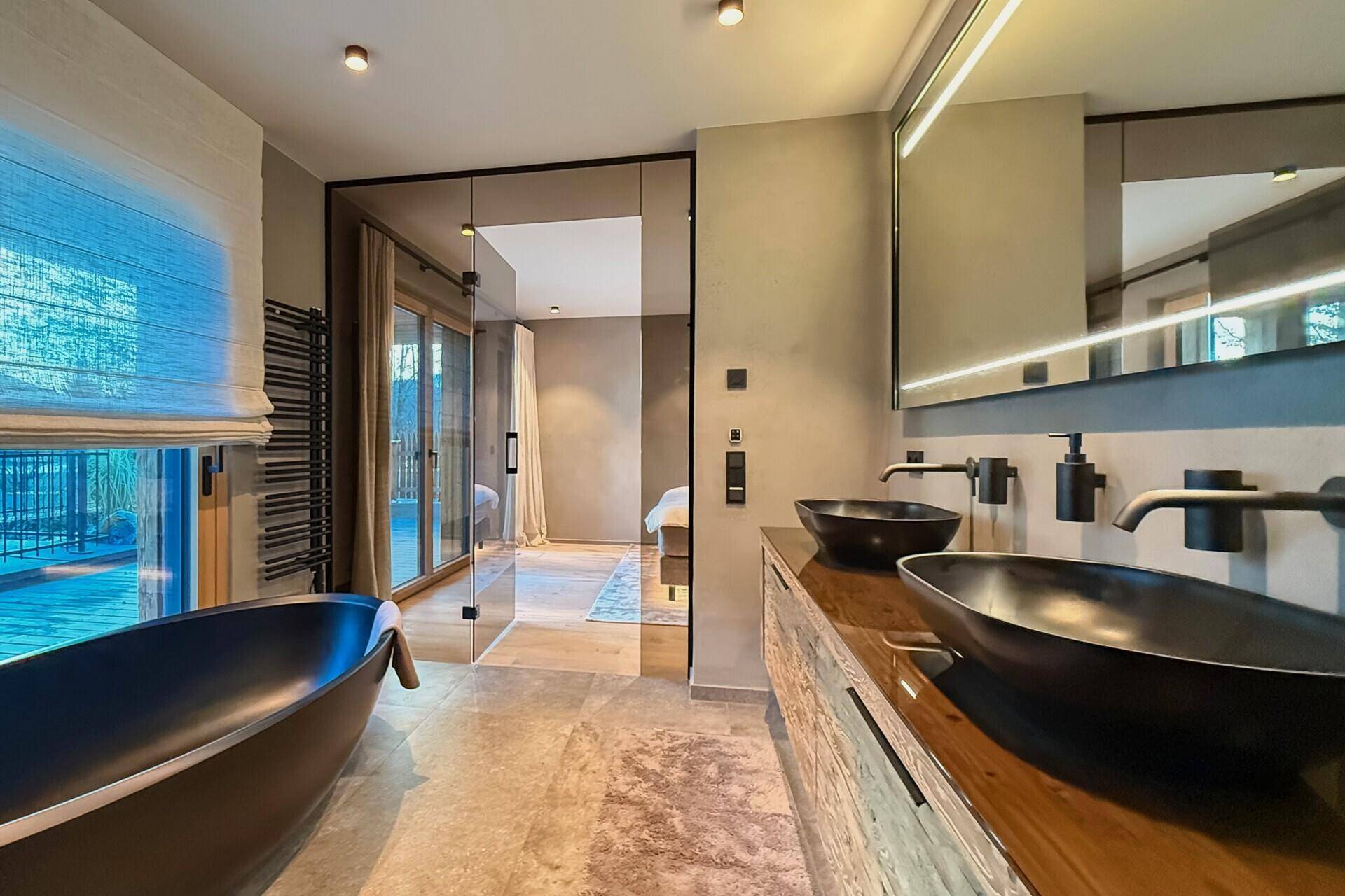 Modernes Badezimmer mit Doppelwaschbecken und Badewanne, offen zum Schlafzimmer.