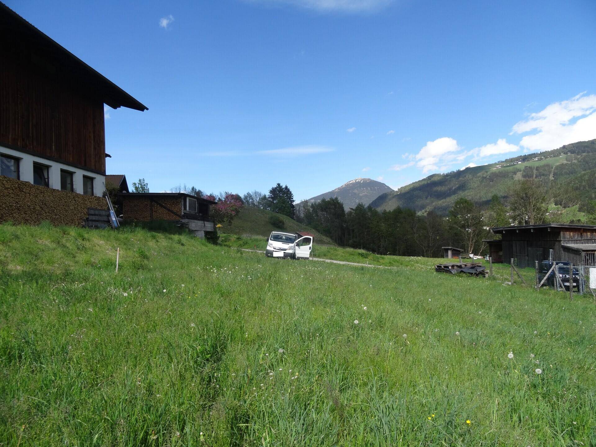 Grüne Landschaft mit Bergen im Hintergrund, einem Gebäude und einem weißen Lieferwagen.
