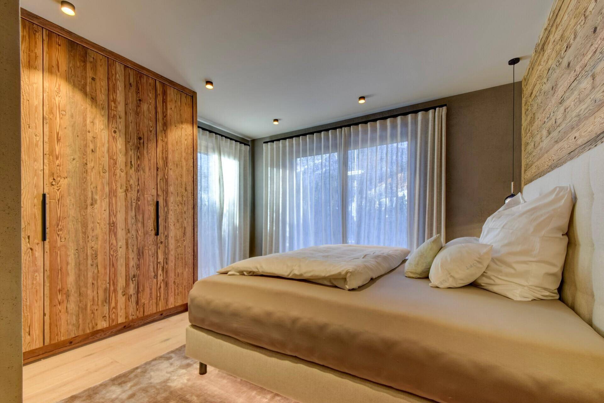 Helles Schlafzimmer mit Holzwänden, Einbauschränken und großen Fenstern mit Vorhängen.