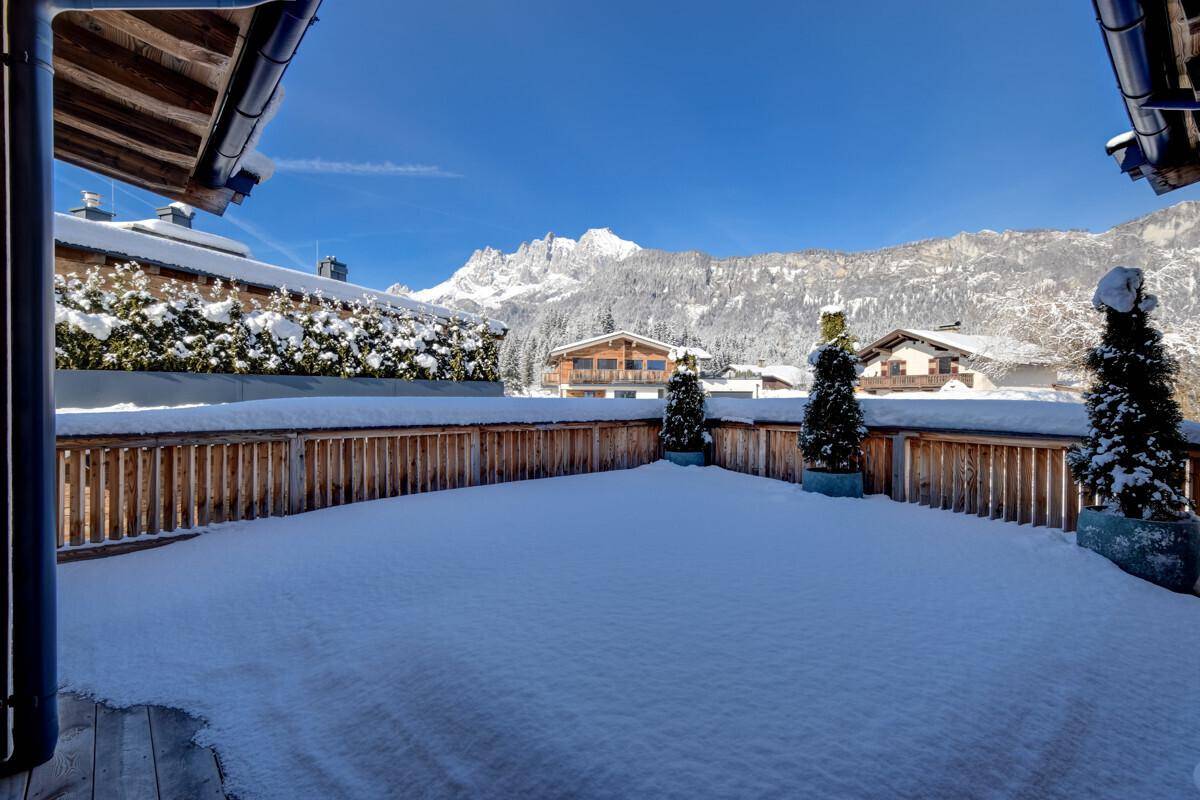 Große, schneebedeckte Terrasse mit Holzzaun und Blick auf die umliegenden Berge.