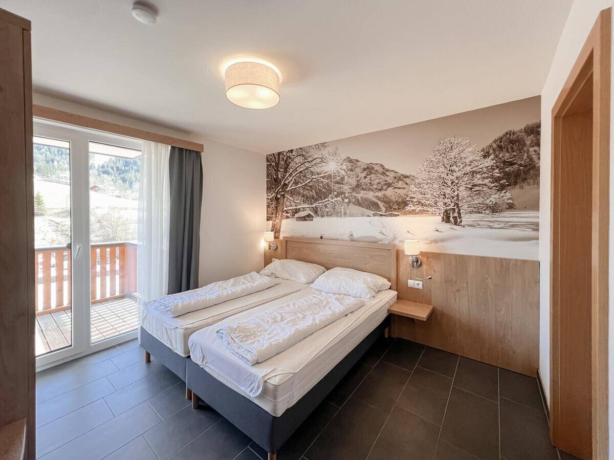 Helles Schlafzimmer mit Doppelbett, dunklen Fliesen und Wandbild mit Winterlandschaft, Zugang zum Balkon.