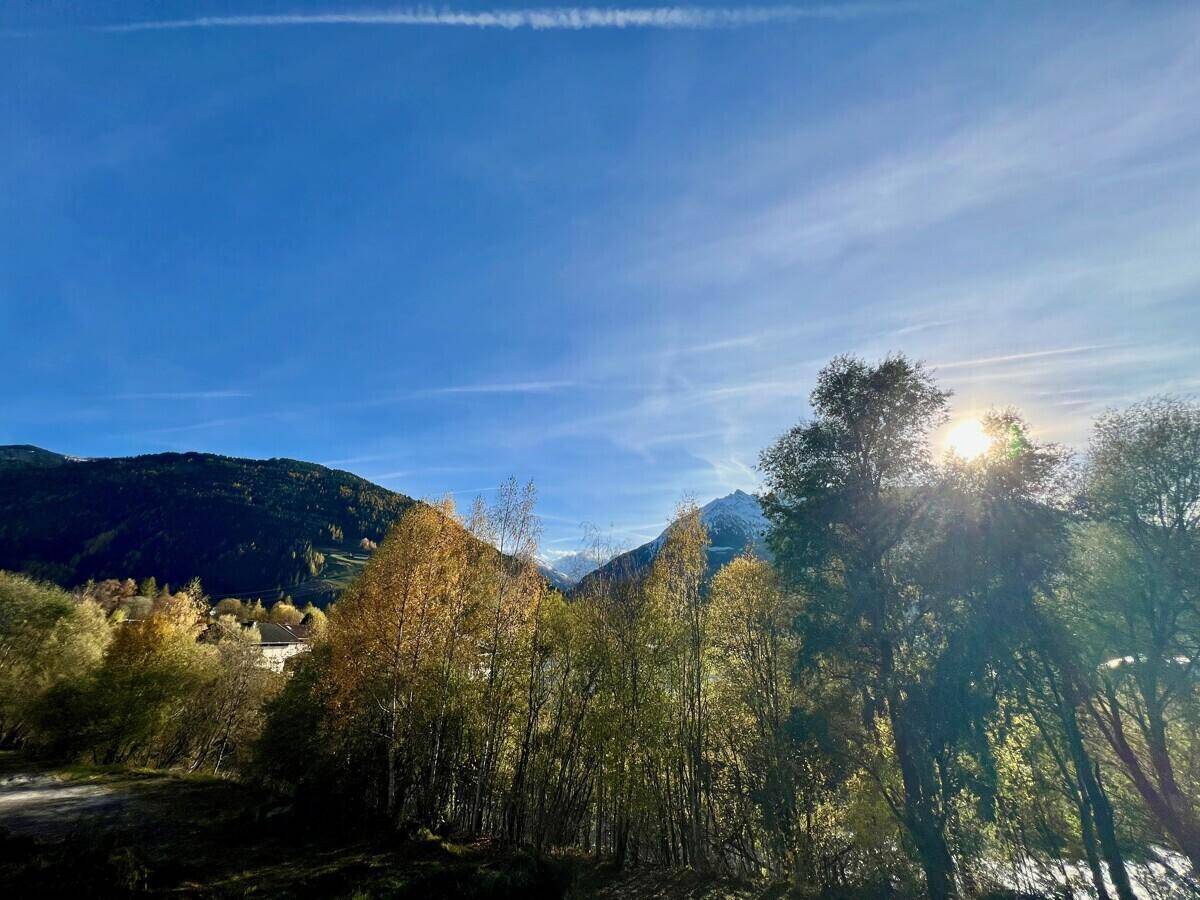 Sonniger Ausblick auf die Berge und herbstliche Bäume mit strahlendem Himmel.