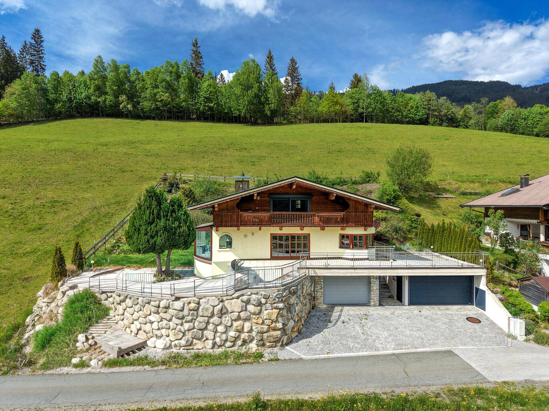 Charmantes Chalet mit traditionellem Holzbalkon und integrierter Garage, umgeben von üppigem Grün.