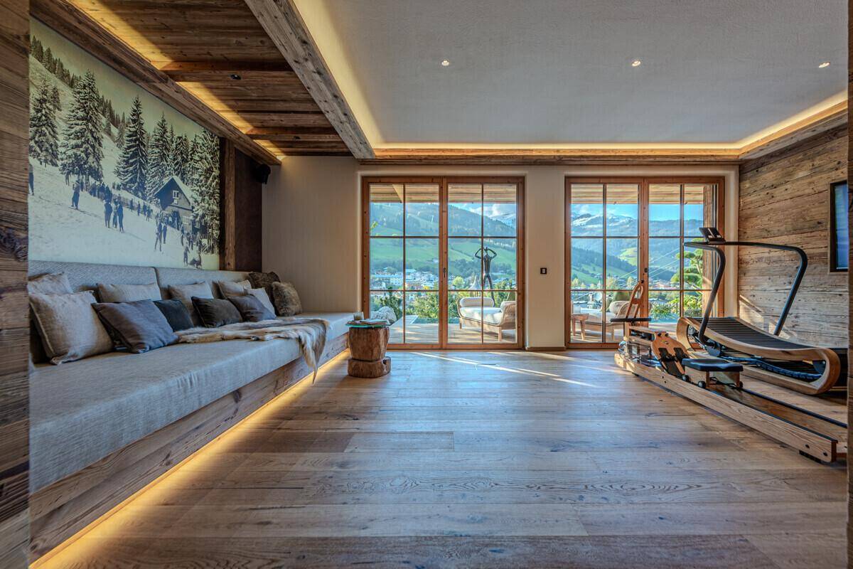 Heller Fitnessraum mit Holzboden, großer Fensterfront und Panoramablick auf die Berge.