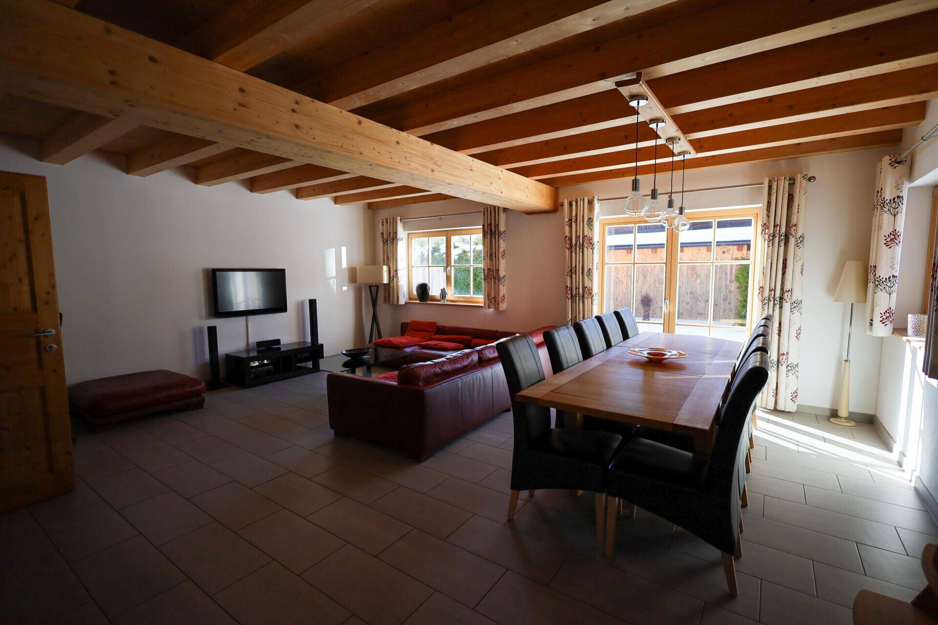 Geräumiger Wohn-Essbereich mit bequemer Ledercouch, großem Esstisch und Holzbalkendecke.
