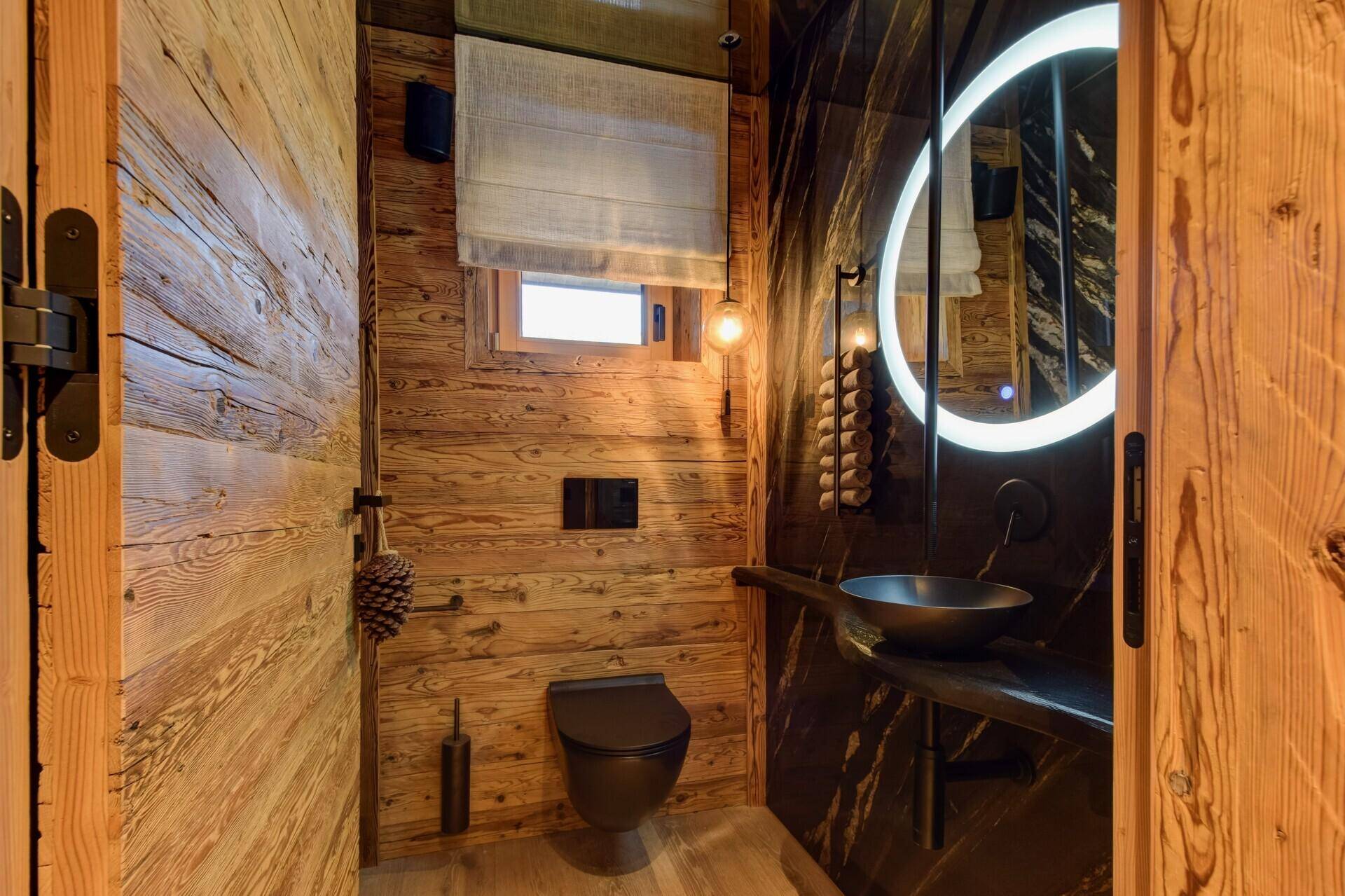 Stilvolles Gäste-WC mit Holzwänden, beleuchtetem Spiegel und modernem Waschbecken.
