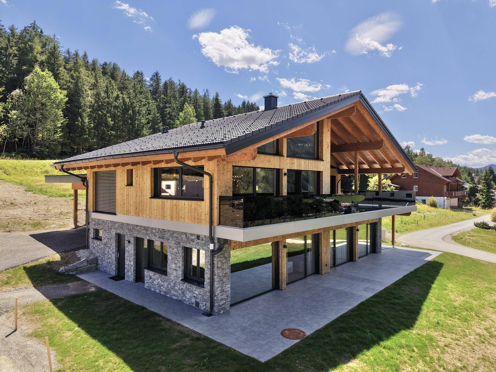 Modernes Chalet mit Holzfassade, Steinelementen und großzügiger Terrasse in alpiner Umgebung.