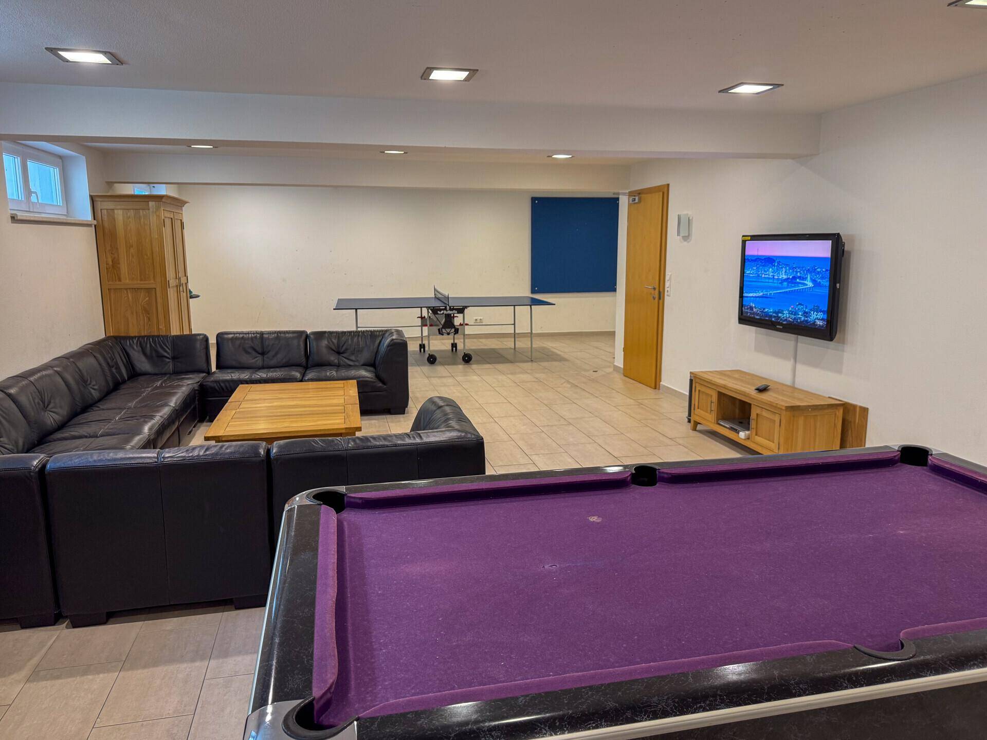 Geräumiger Spielraum mit Billardtisch, Tischtennisplatte und gemütlicher Sitzecke.