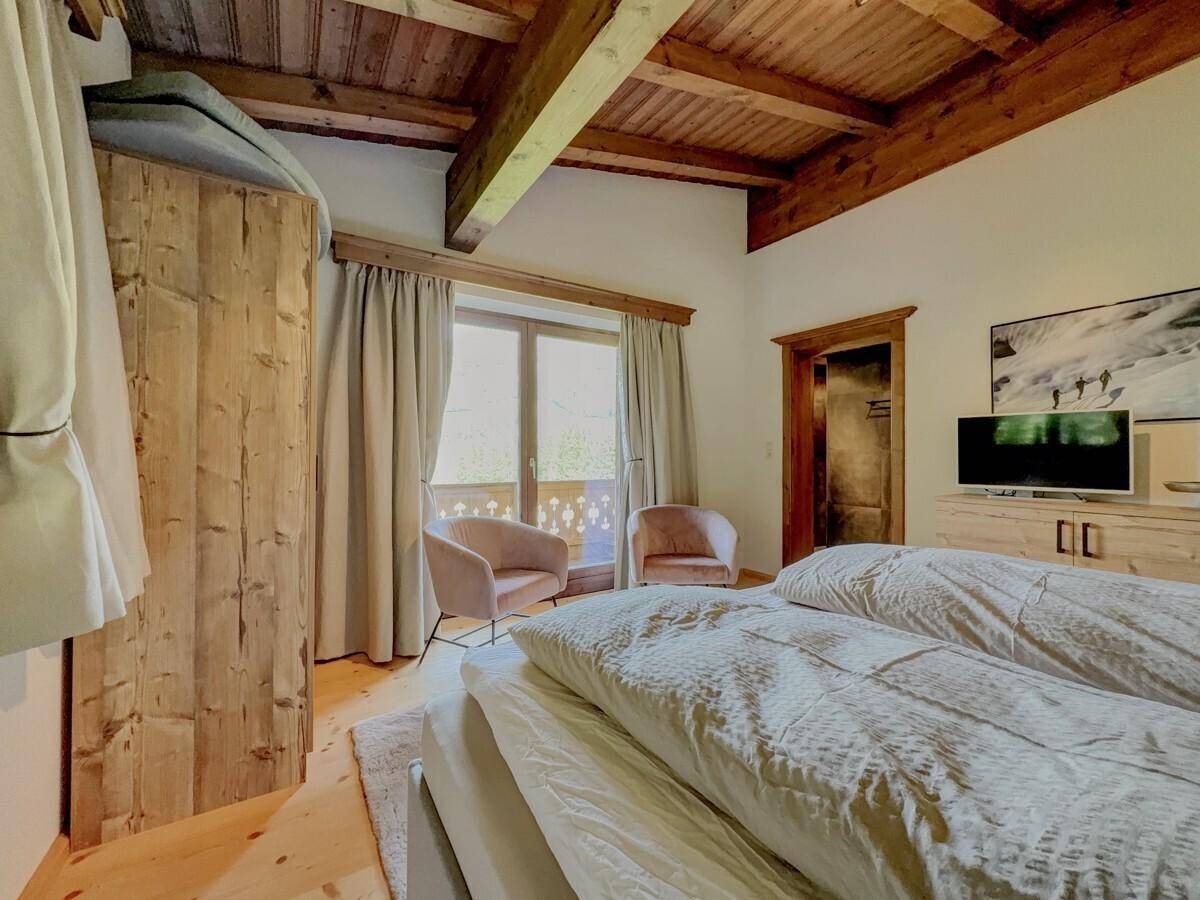 Schlafzimmer mit Holzbalkendecke, TV und Zugang zum Balkon mit Bergblick.