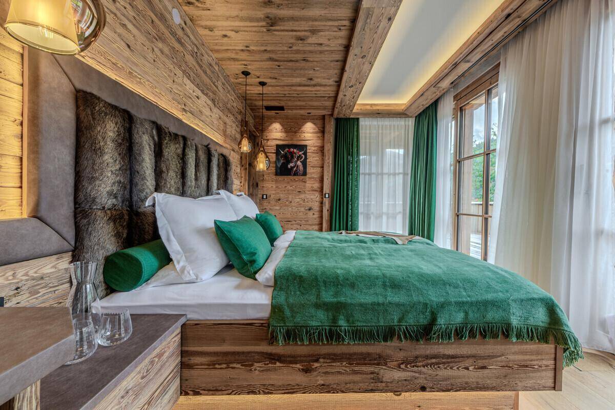 Gemütliches Schlafzimmer im alpinen Stil mit Holzwänden, grünen Akzenten und einem bequemen Bett.