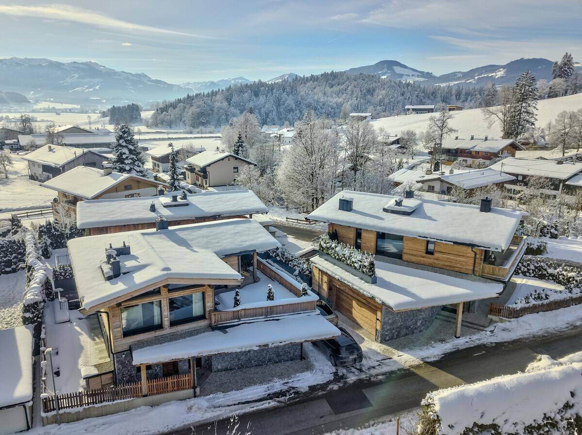 Winterliche Luftaufnahme einer Siedlung von modernen Chalets in einer verschneiten Landschaft.