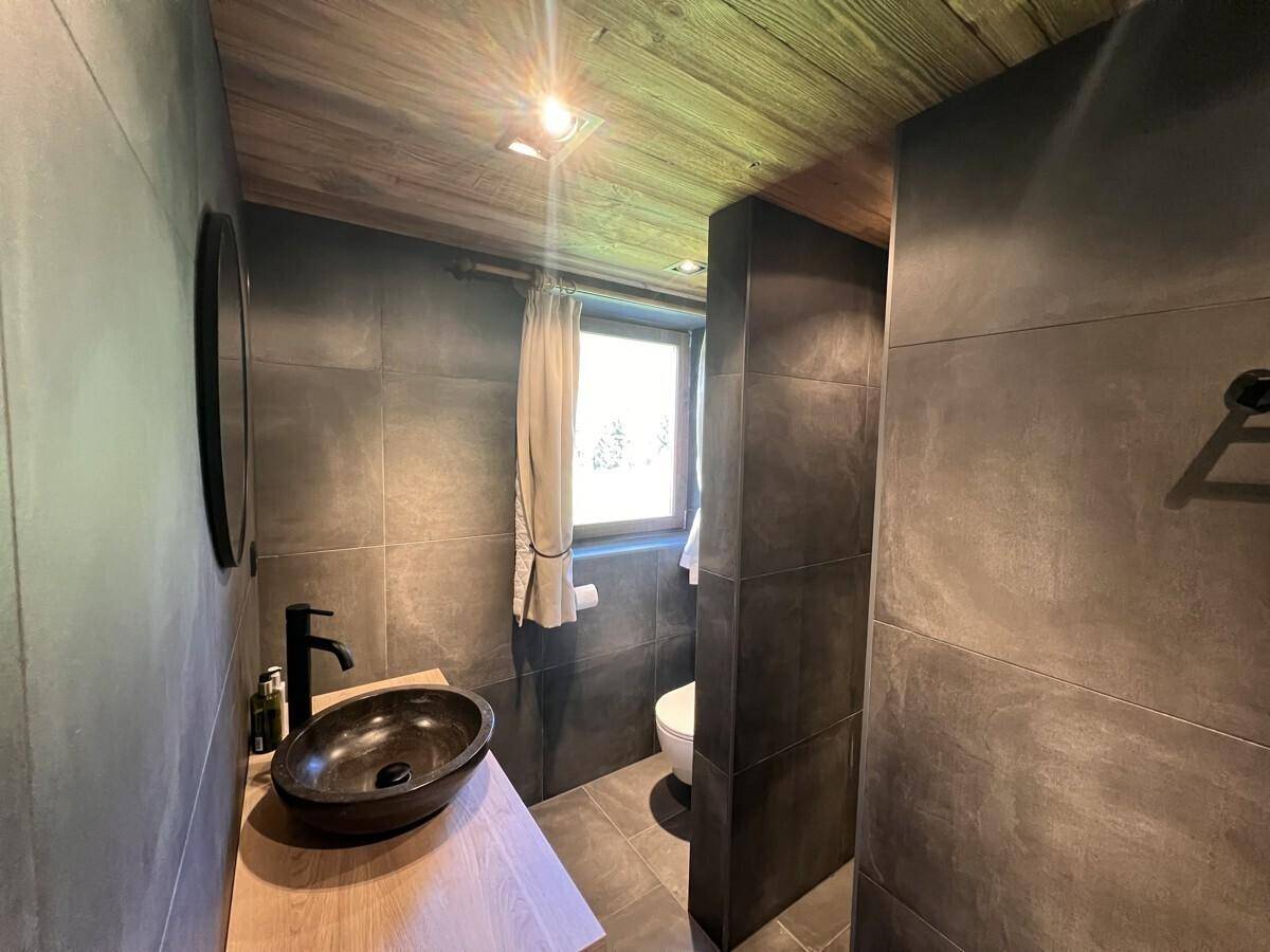 Modernes Badezimmer mit dunklen Fliesen, Holzwaschtisch und begehbarer Dusche.
