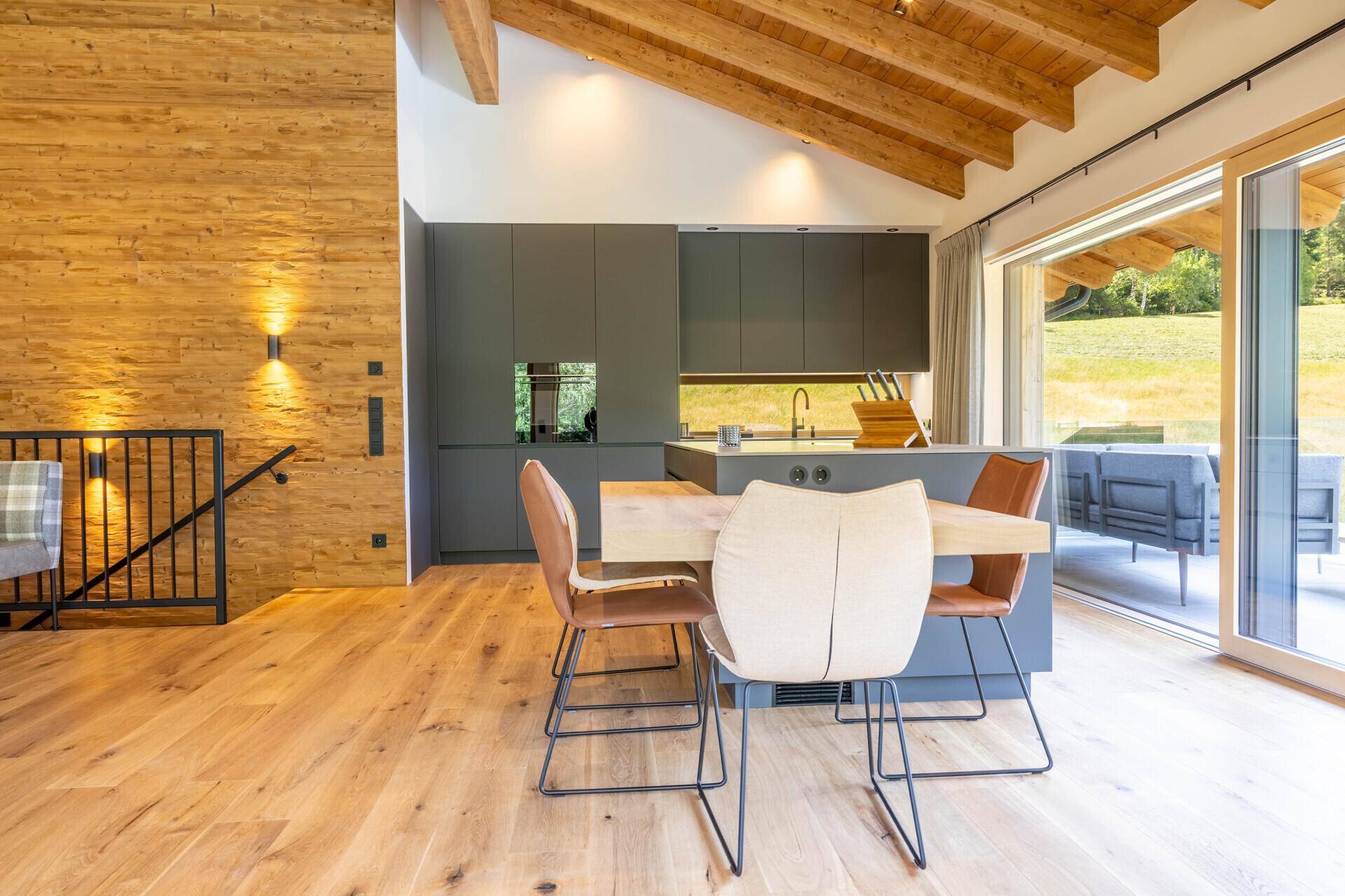 Offene Küche mit Essbereich, Holzboden und Zugang zur Terrasse mit Bergblick.