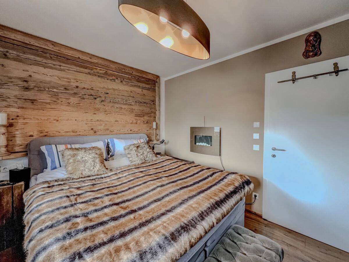 Helles Schlafzimmer im Chalet-Stil mit Holzwand, großem Bett und modernem Wandkamin.
