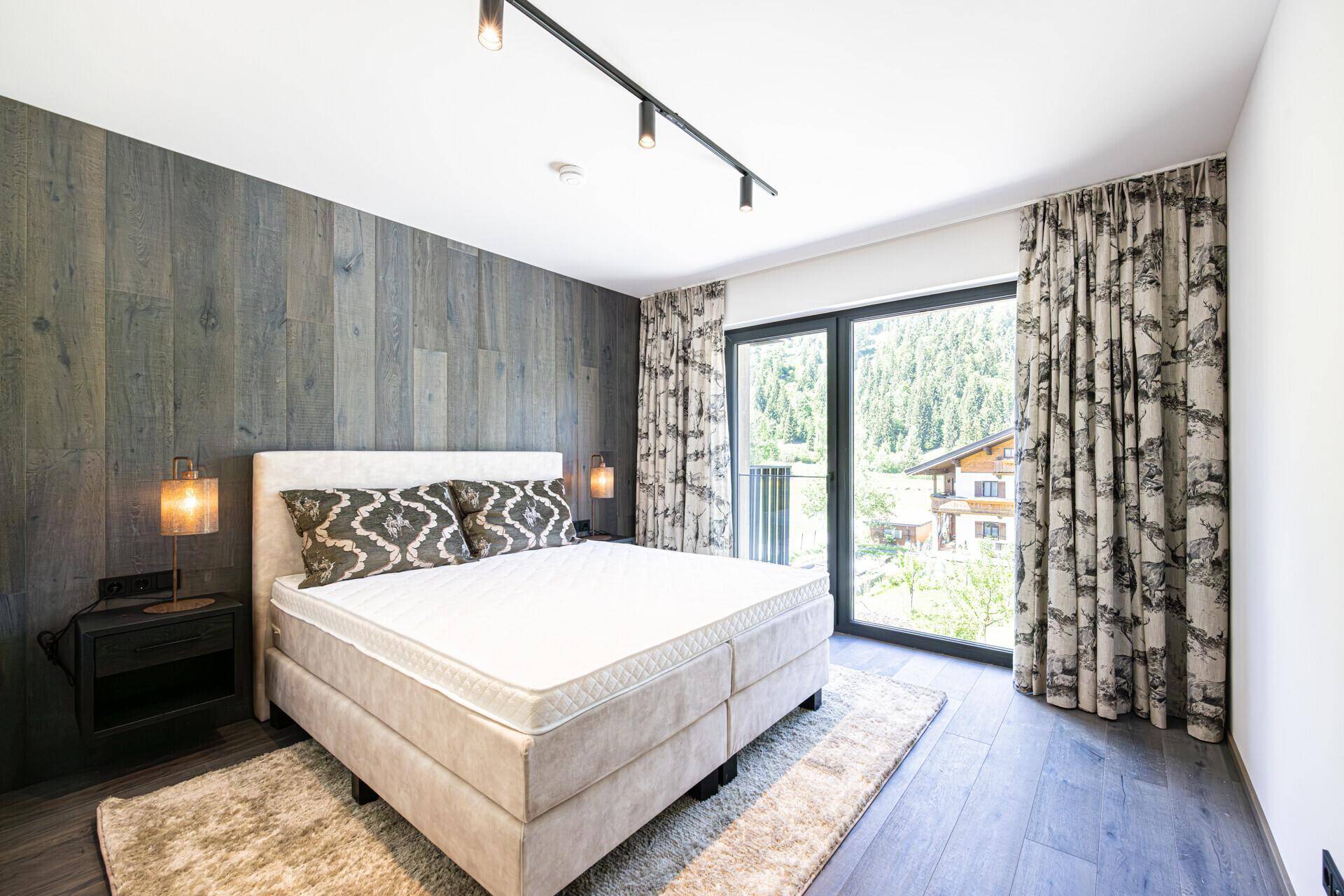Helles Schlafzimmer mit Doppelbett, Holzwand und Balkonzugang mit Blick ins Grüne.