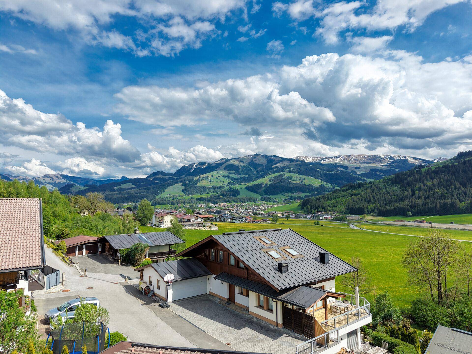 Traditionelles Haus mit Satteldach und umliegenden Gebäuden, vor der Kulisse schneebedeckter Berge.