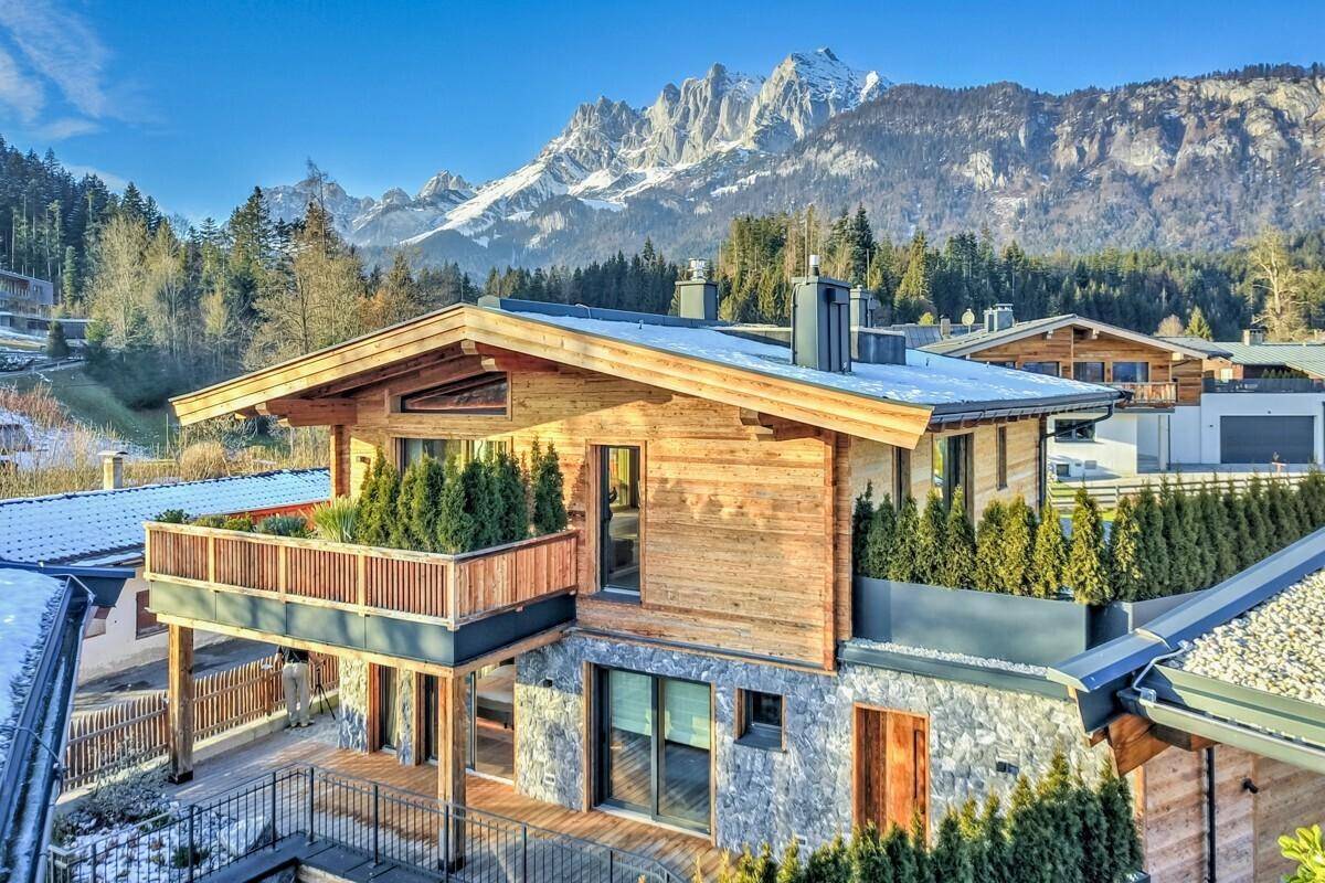 Attraktives Holzchalet mit Steinfassade und Balkon, umgeben von verschneiten Bergen.