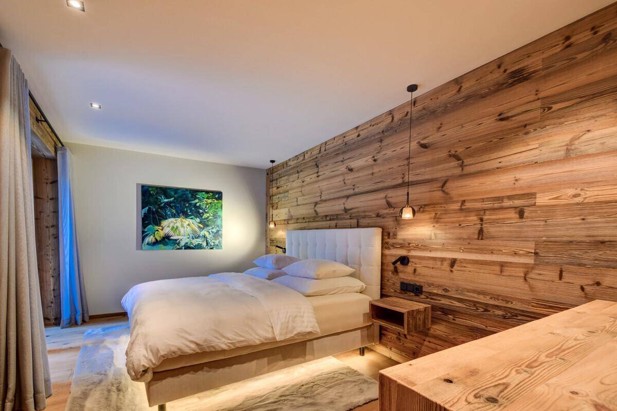 Gemütliches Schlafzimmer mit Holzwand, indirekter Beleuchtung und Blick ins Grüne.