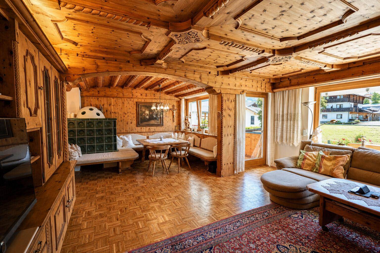Traditioneller Wohn- und Essbereich im alpinen Stil mit viel Holz, Kachelofen und Blick ins Grüne.