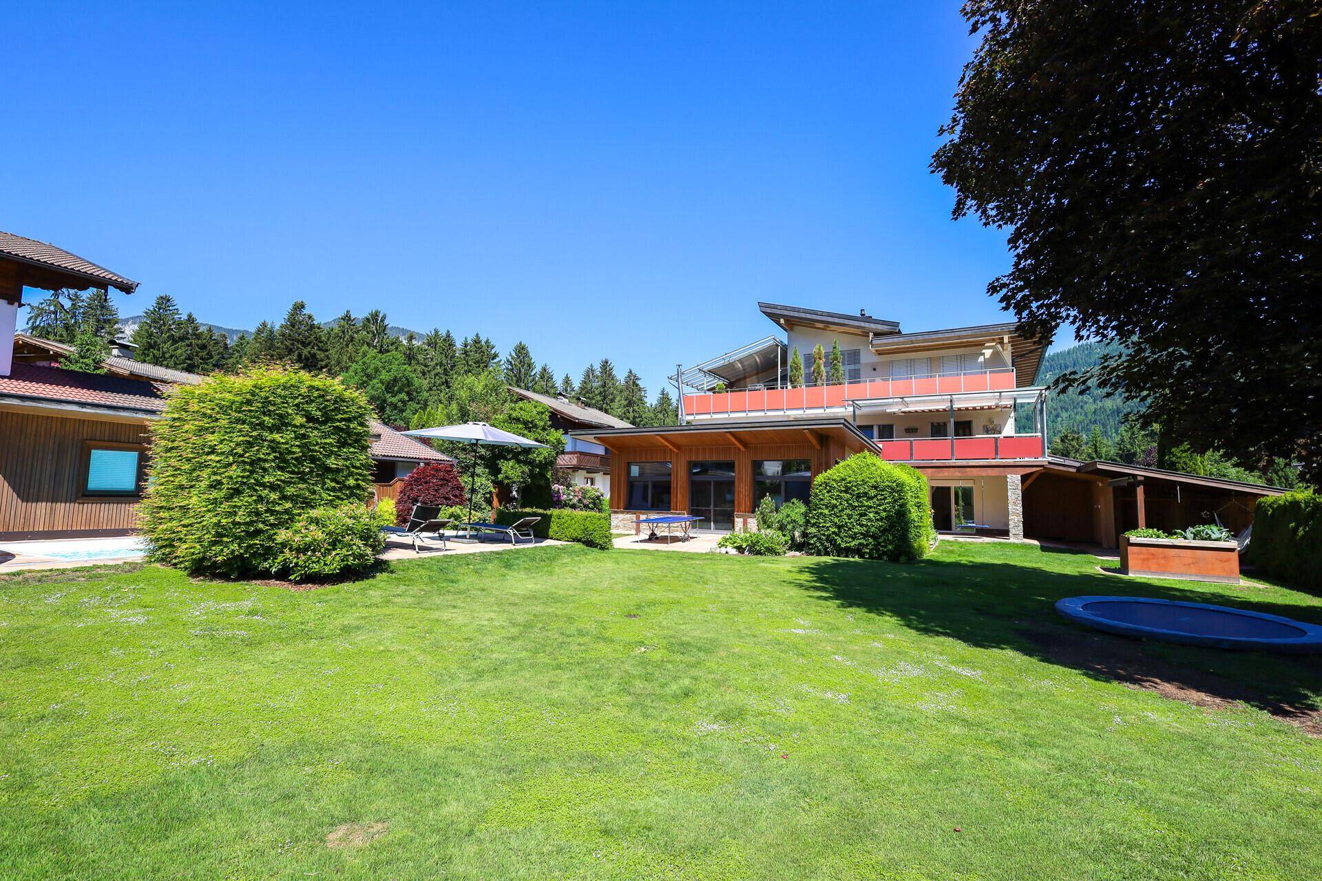 Weitläufiger Garten mit Rasenfläche, Bäumen und einem modernen Haus im Hintergrund.