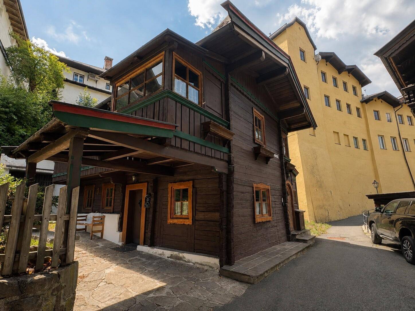 Seitenansicht des Holzhauses mit überdachtem Eingangsbereich und Steinweg, umgeben von Bäumen.