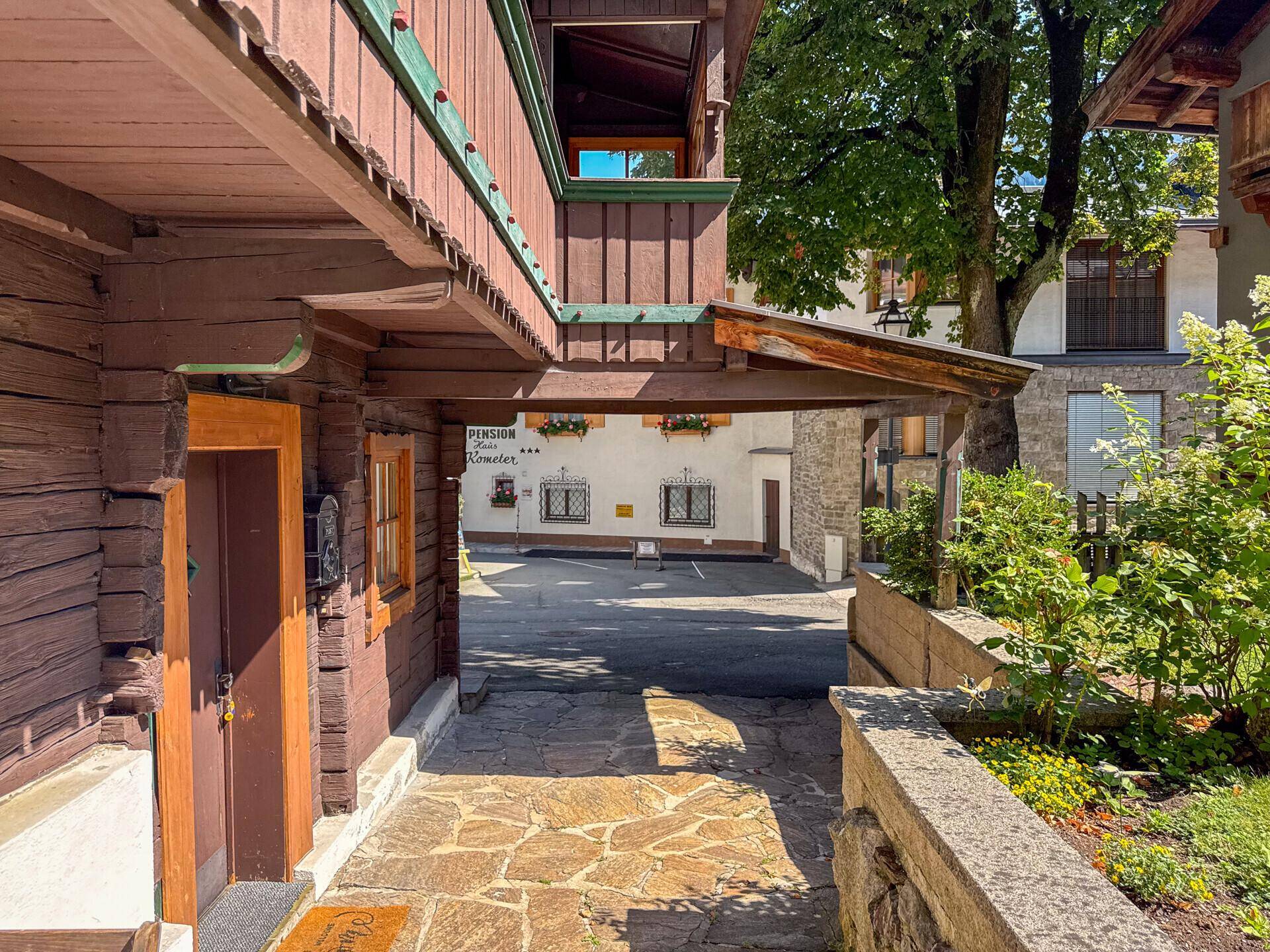 Eingangsbereich eines traditionellen Holzhauses mit Steinweg und Blick auf die Straße.
