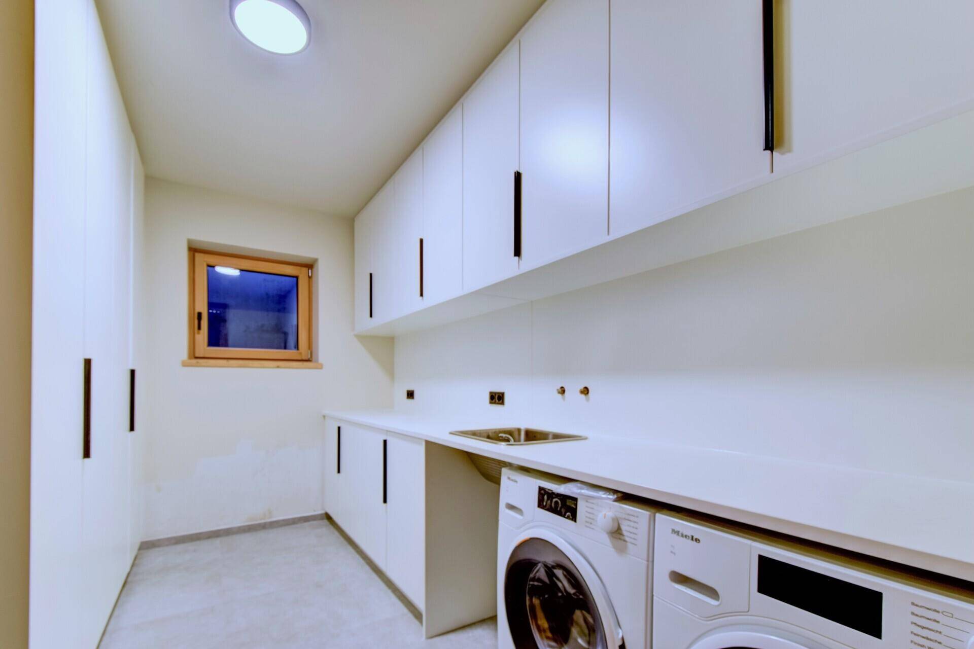 Heller Hauswirtschaftsraum mit Waschmaschine, Trockner und viel Stauraum in weißen Schränken.