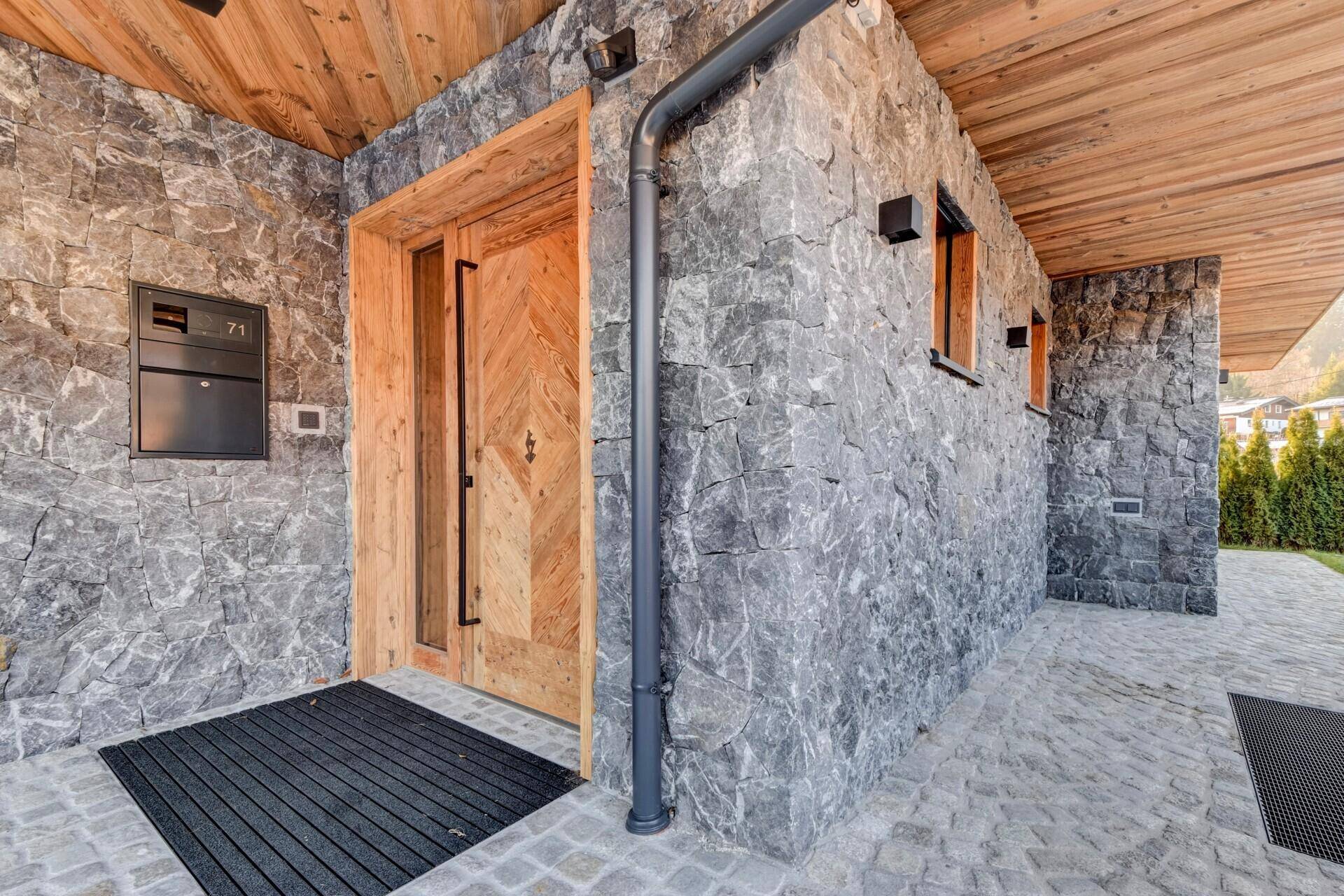 Eingangsbereich des Hauses mit Steinfassade und Holztür, einladend und robust gestaltet.