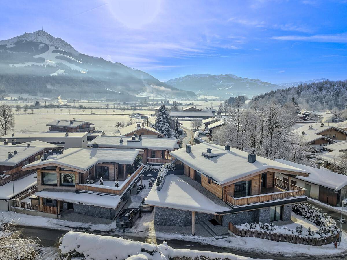 Winterliche Luftaufnahme einer Siedlung von modernen Chalets in einer verschneiten Landschaft.