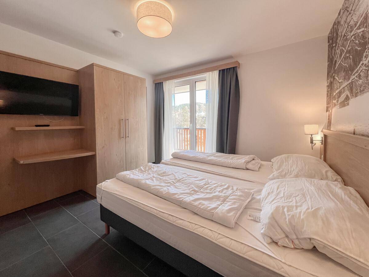 Schlafzimmer mit Doppelbett, integriertem TV-Bereich und Holzschrank, mit Balkonzugang.