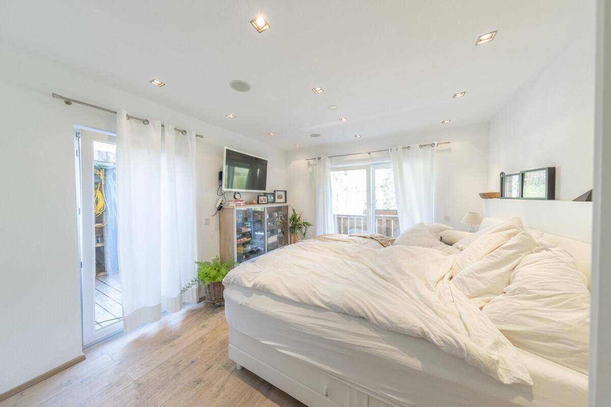 Helles Schlafzimmer mit Doppelbett, Holzboden und Zugang zu einem begehbaren Kleiderschrank.