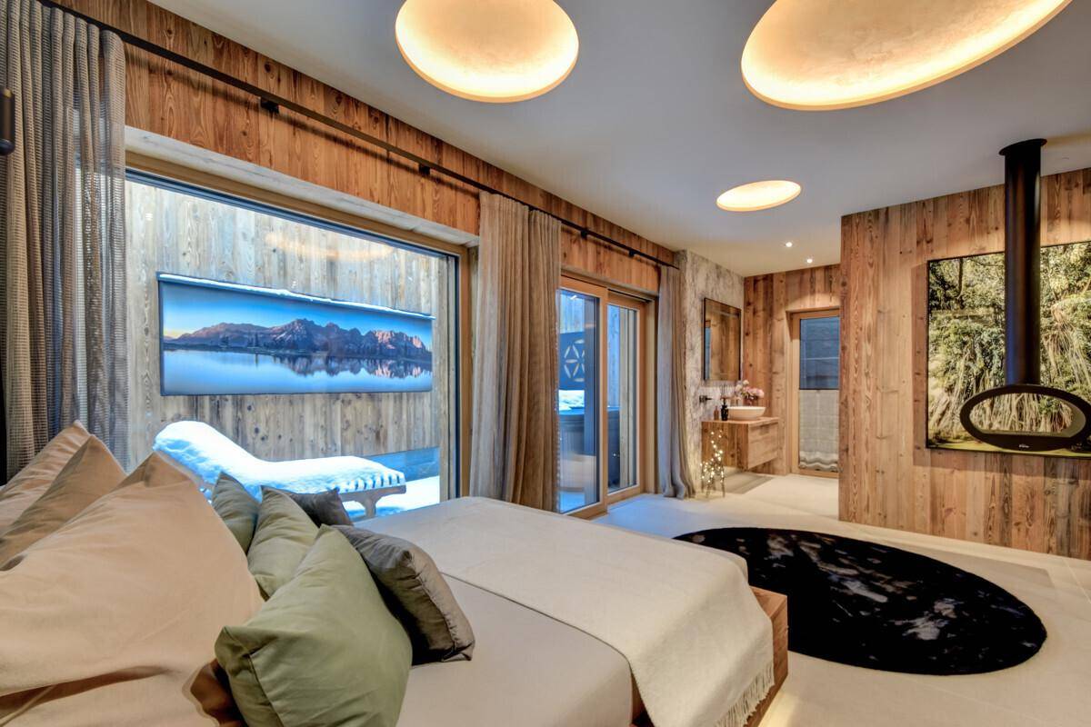 Helles Schlafzimmer mit Holzbett, Kamin und Zugang zum Außenbereich.