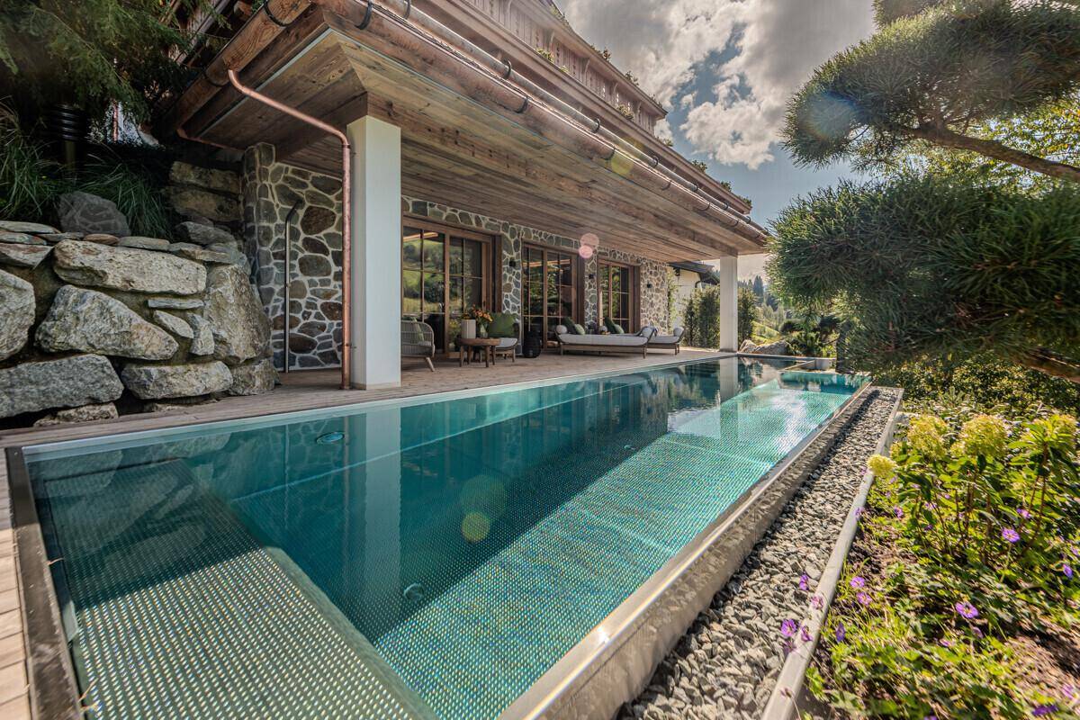 Außenbereich mit langem Infinity-Pool, umgeben von Naturstein und üppiger Bepflanzung.