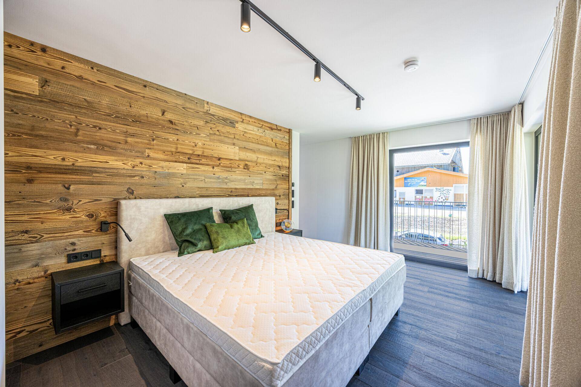 Modernes Schlafzimmer mit Holzwand, Balkonzugang und Blick auf die umliegende Landschaft.