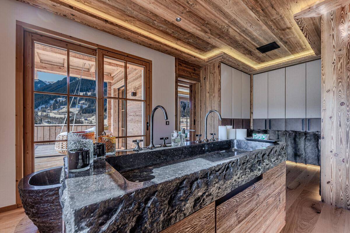 Exklusives Badezimmer mit Doppelwaschbecken aus Stein, Holzelementen und Bergblick.