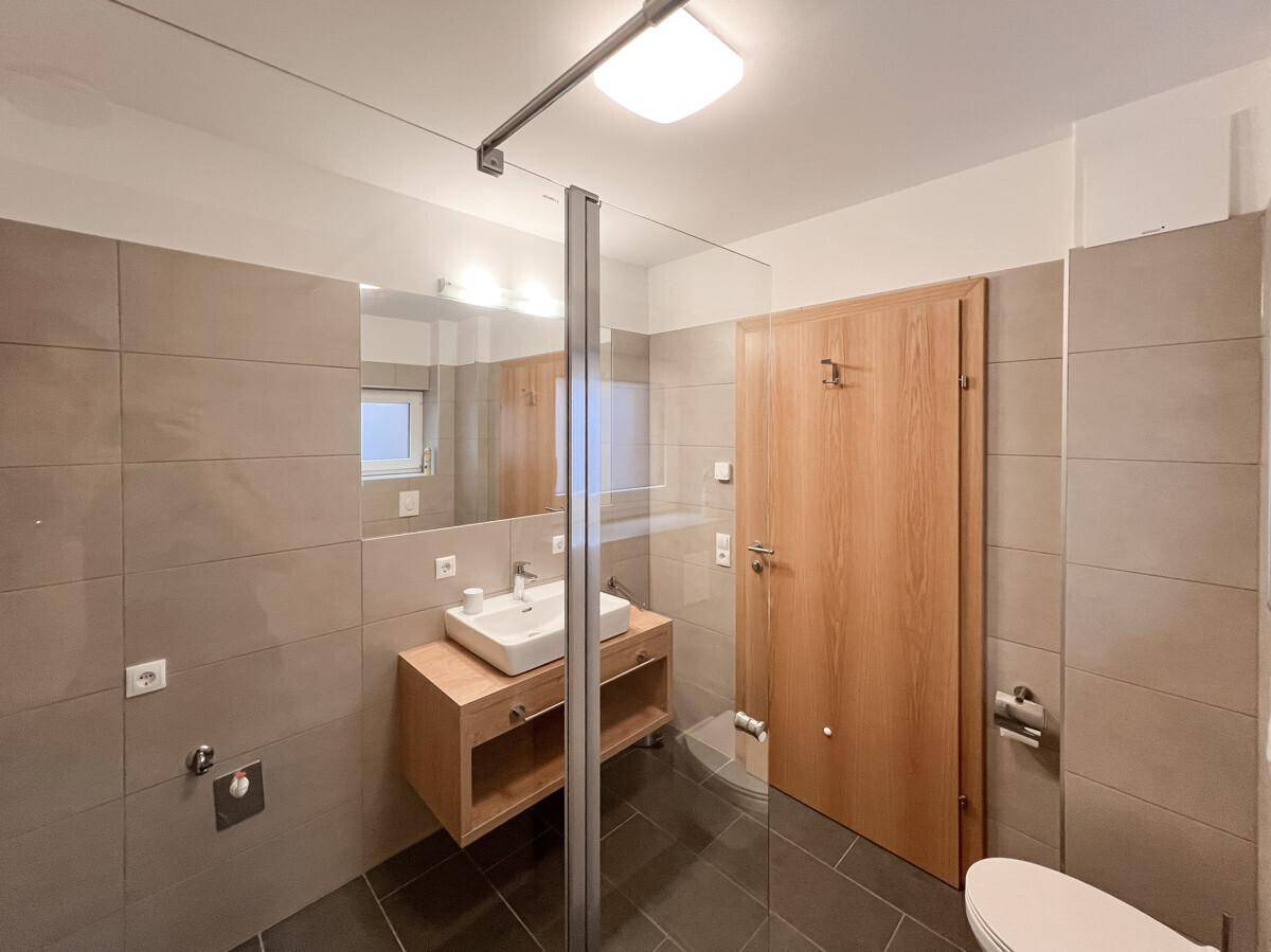 Modernes Badezimmer mit großformatigen Fliesen, Einzelwaschbecken und einer begehbaren Dusche.