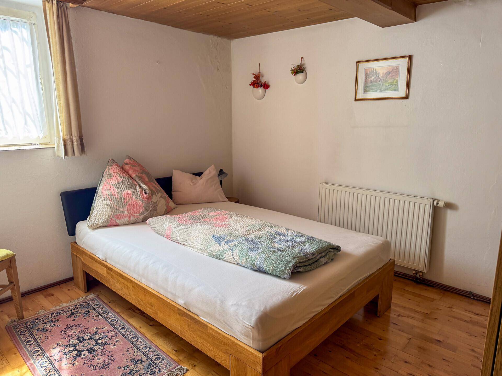 Helles Schlafzimmer mit Holzbettrahmen, Heizkörper und Holzbalkendecke, bietet eine gemütliche Atmosphäre.