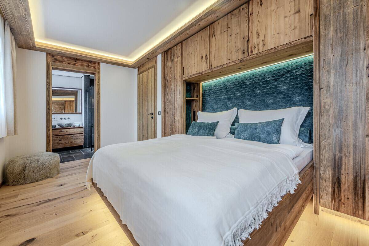 Gemütliches Schlafzimmer im alpinen Stil mit Holzwänden, Einbauschränken und direktem Badzugang.