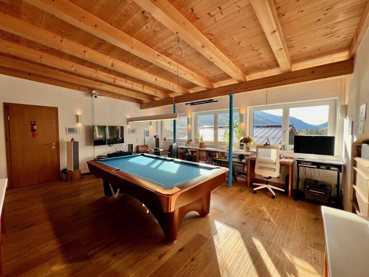 Großes Spielzimmer mit Billardtisch, Holzbalkendecke und Arbeitsbereich am Fenster mit Bergblick.