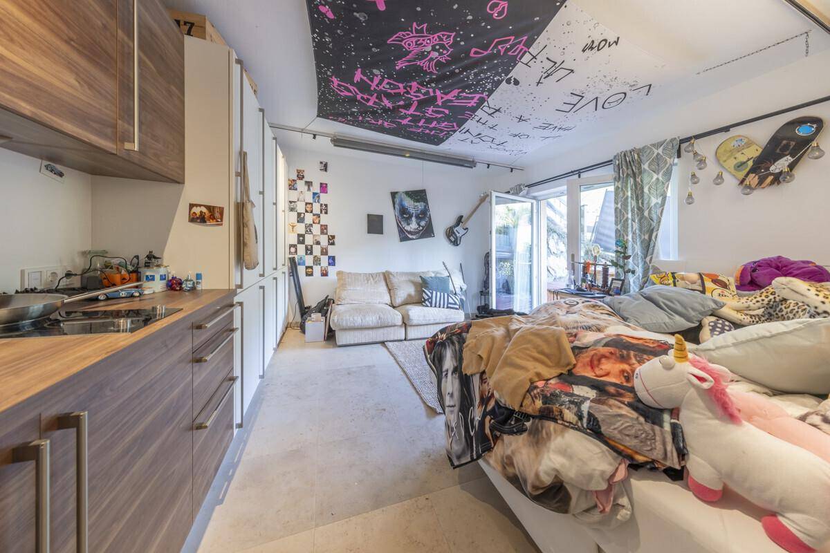 Individuell gestaltetes Schlafzimmer mit Bett, Sofa, Kochnische und Zugang zum Außenbereich.