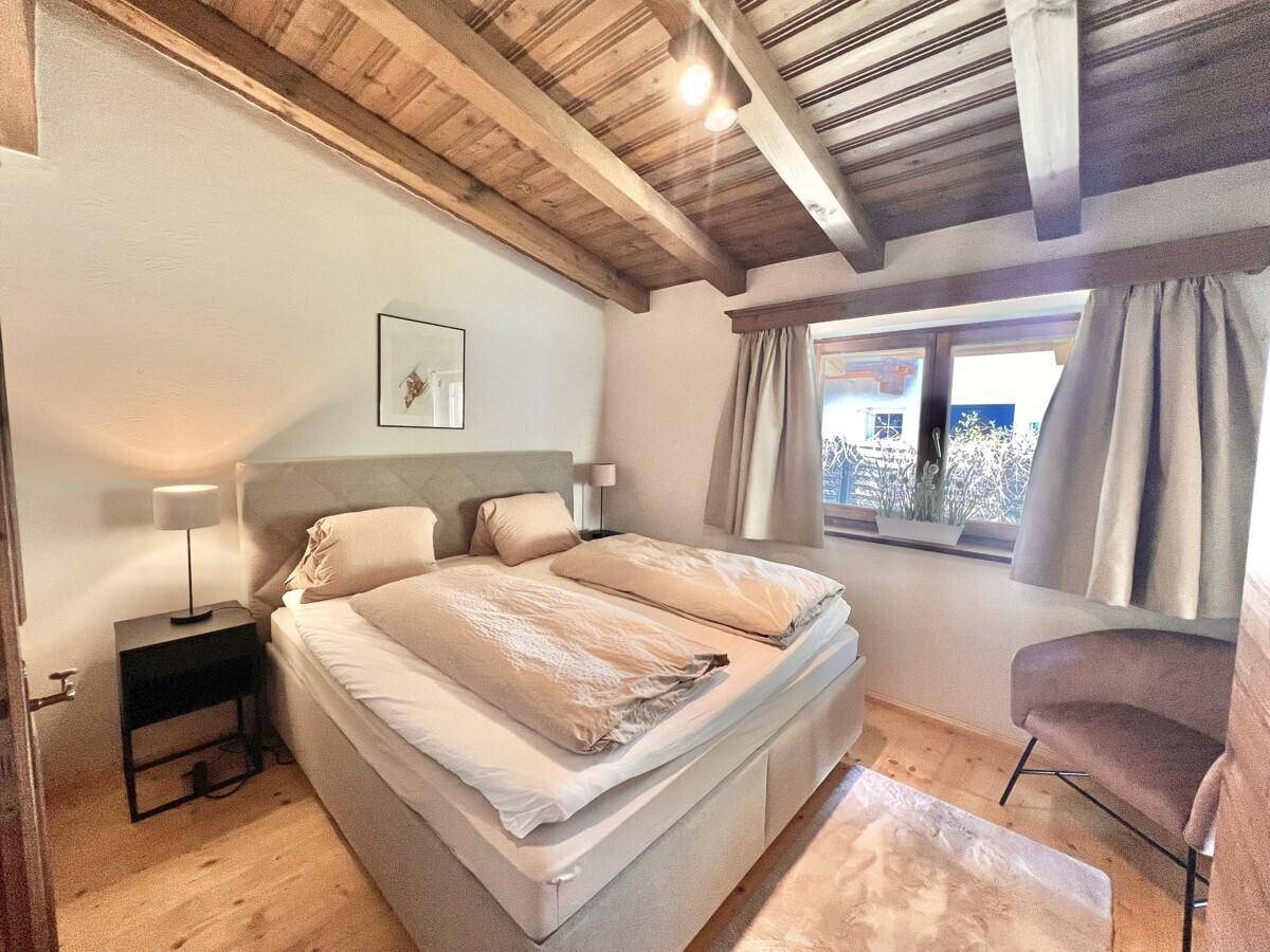 Schlafzimmer mit Holzbalkendecke, Doppelbett und einem Fenster, das viel Tageslicht hereinlässt.