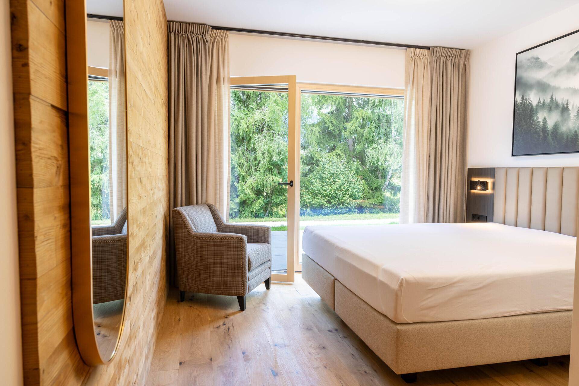 Schlafzimmer mit Holzwand, Sessel und Zugang zu einem Balkon oder Gartenbereich.