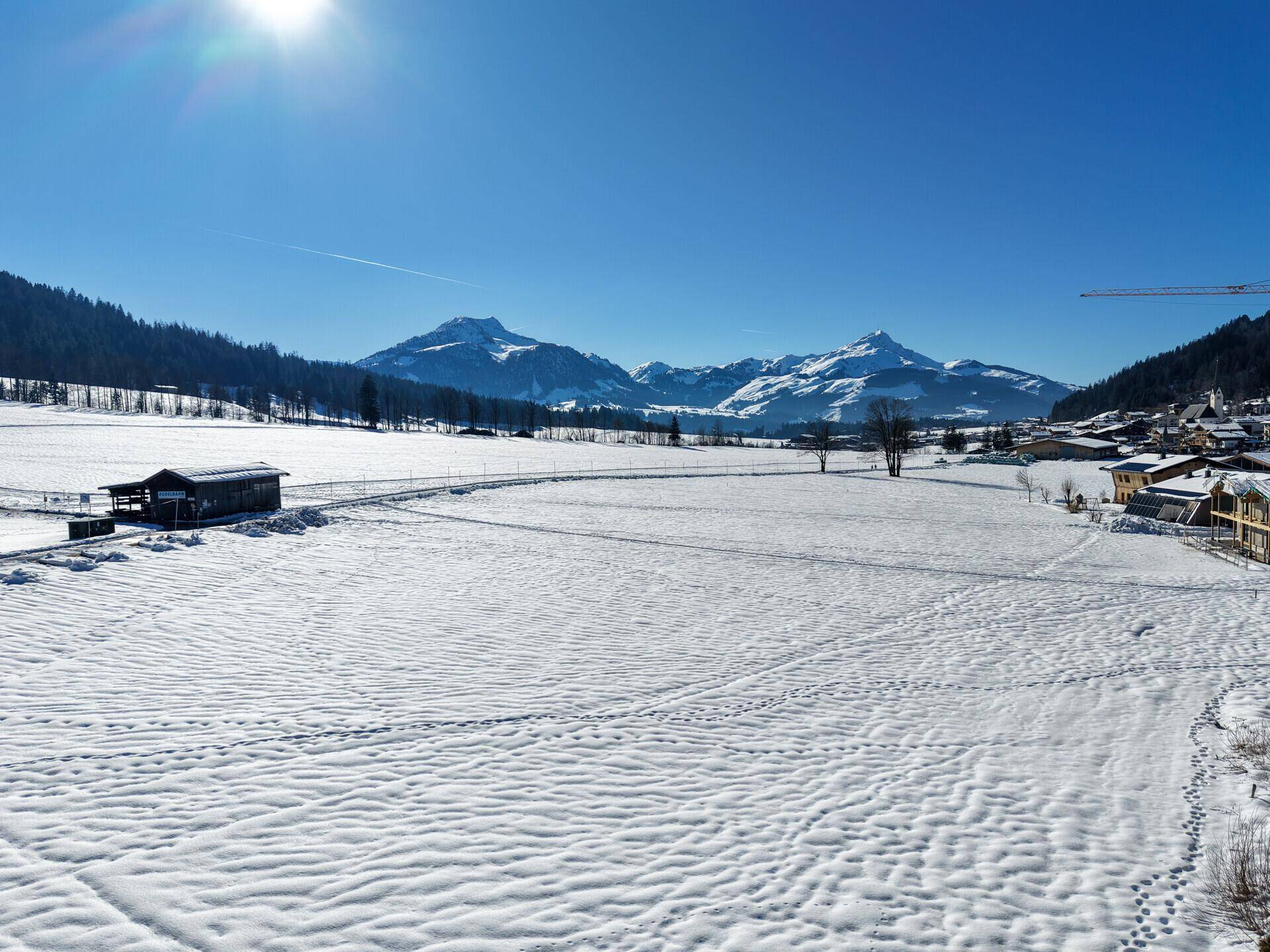 Weitläufiges, verschneites Feld mit majestätischen Bergen am Horizont unter strahlend blauem Himmel.