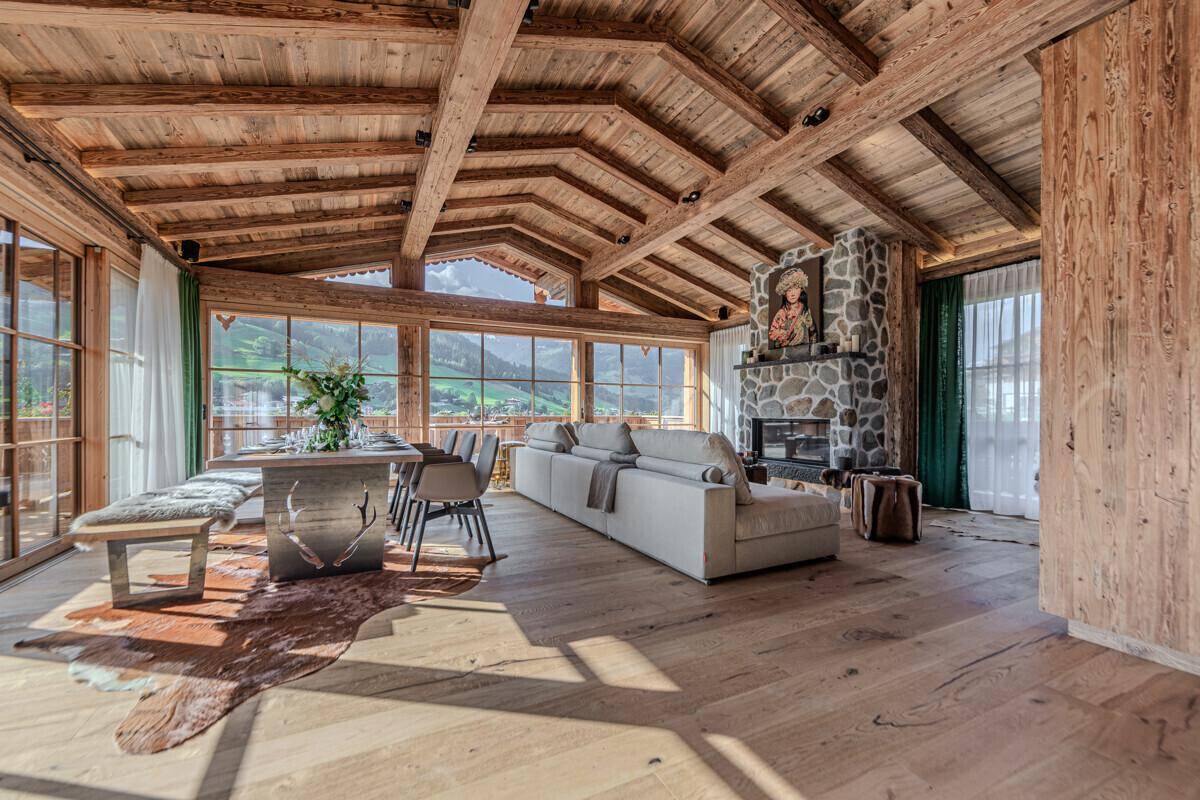Geräumiger Wohn-Essbereich im alpinen Stil mit Holzbalkendecke, Kamin und großen Fenstern mit Bergblick.