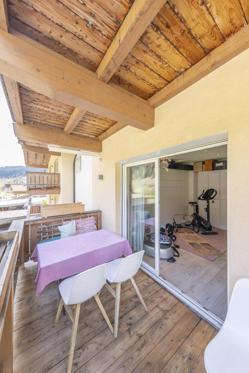 Überdachter Holzbalkon mit Tisch und Stühlen, angrenzend an einen Fitnessraum.