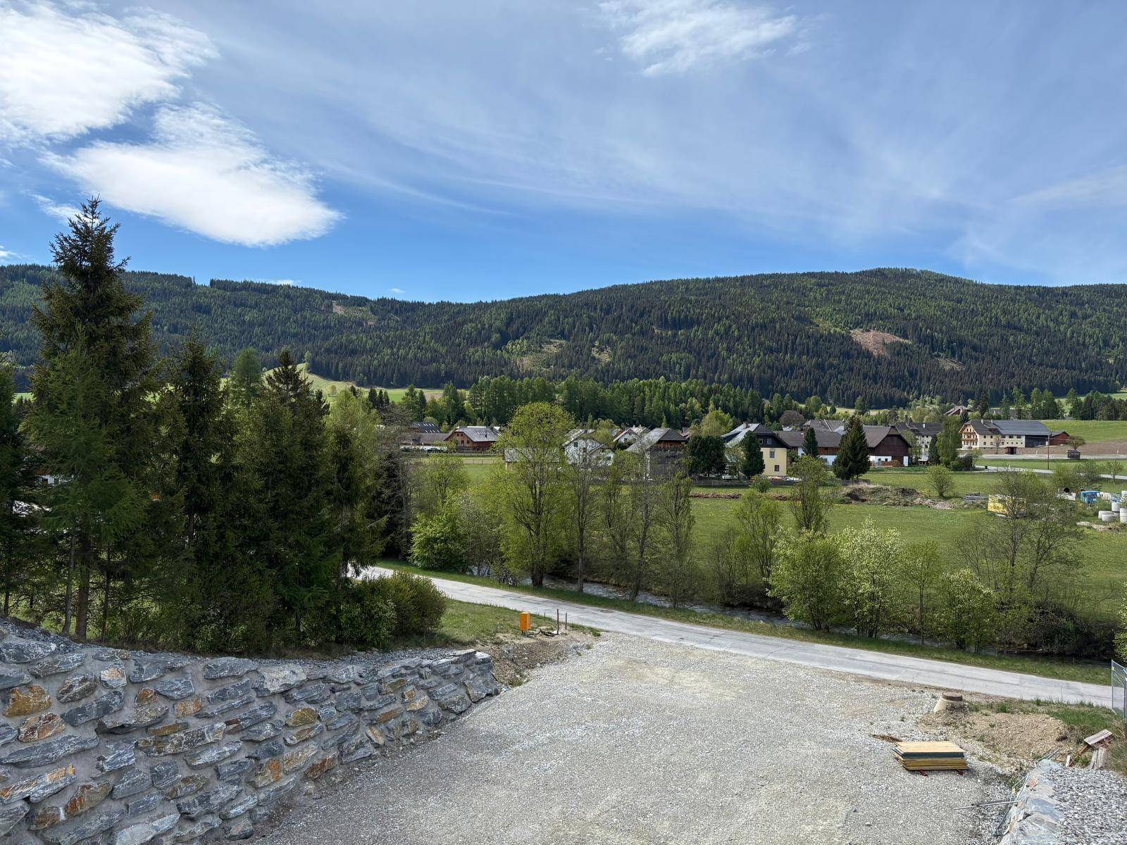 Weitläufige Landschaft mit ländlicher Bebauung, grünen Wiesen und bewaldeten Hügeln unter blauem Himmel.