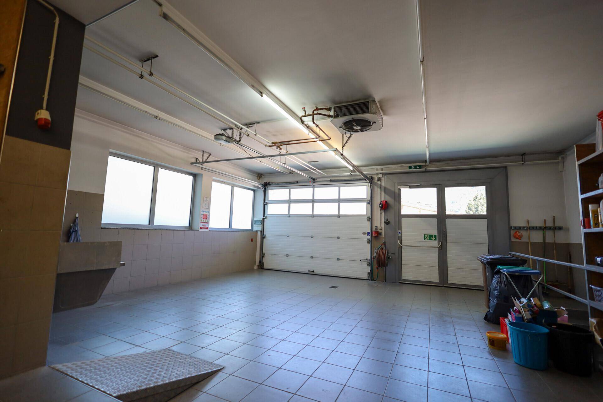 Geräumige und helle Garage mit Fliesenboden, Fenstern und großem Rolltor für mehrere Fahrzeuge.