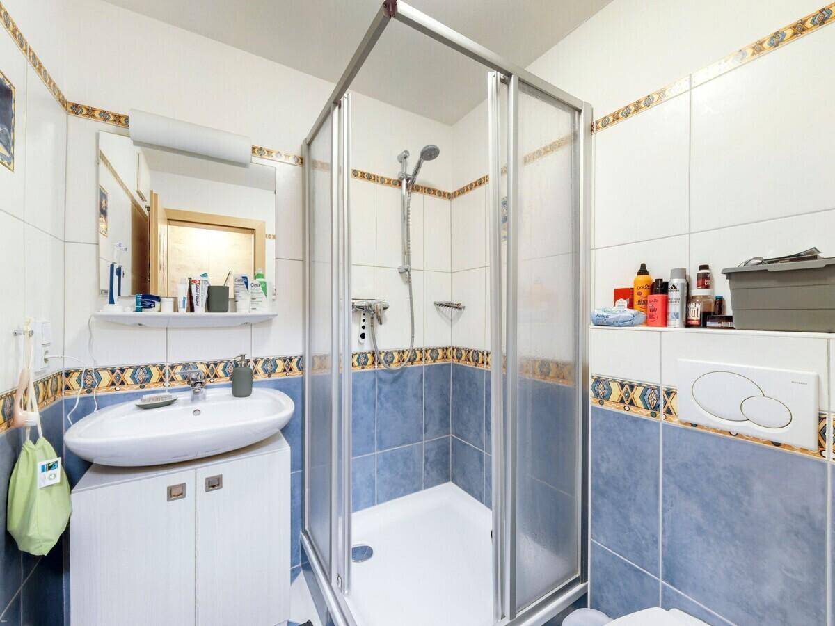 Badezimmer mit Duschkabine, Einzelwaschbecken und dekorativen blau-weißen Fliesen.