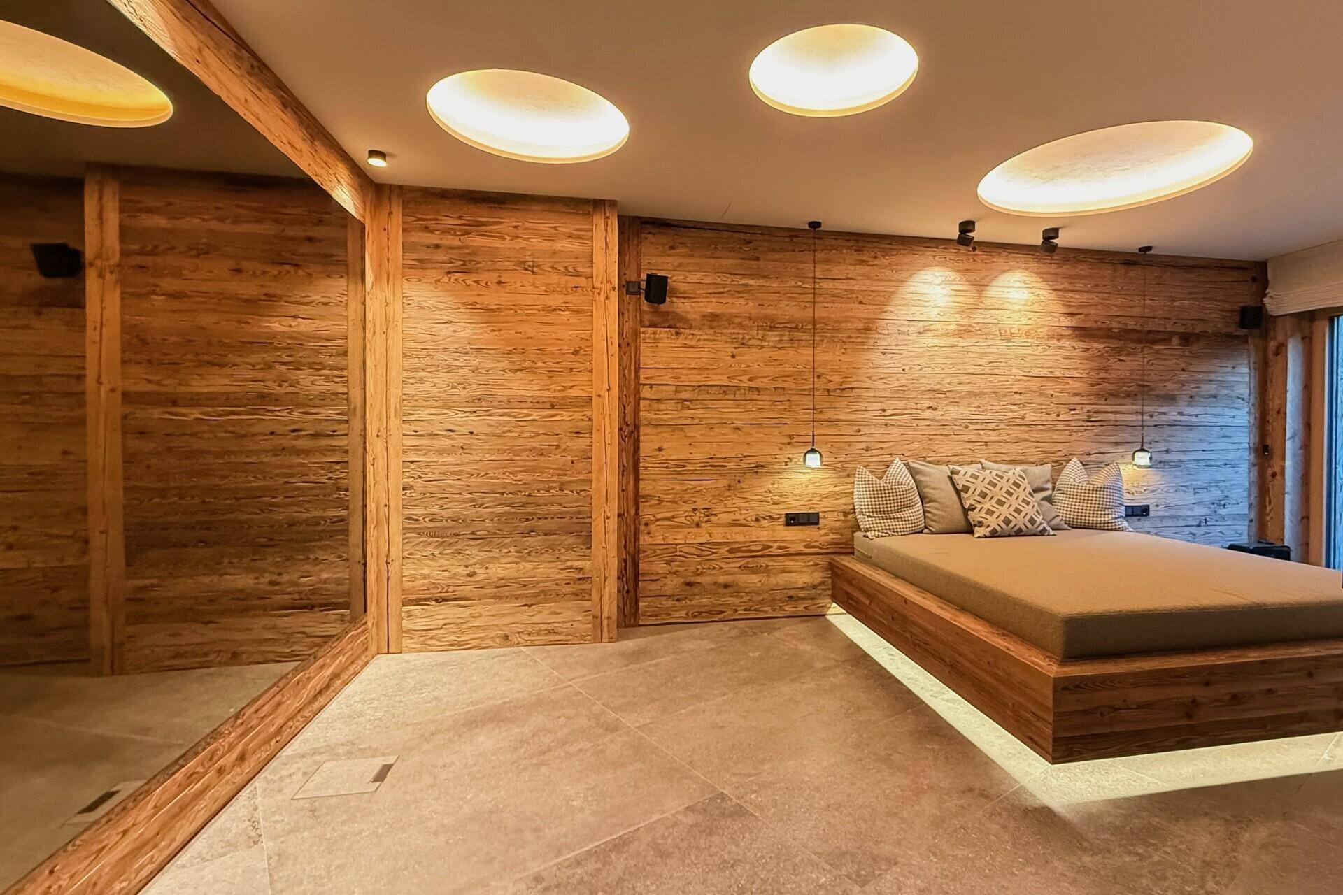 Schlafzimmer mit Holzwänden, Holzbett und runden Deckenleuchten, warm beleuchtet und einladend.